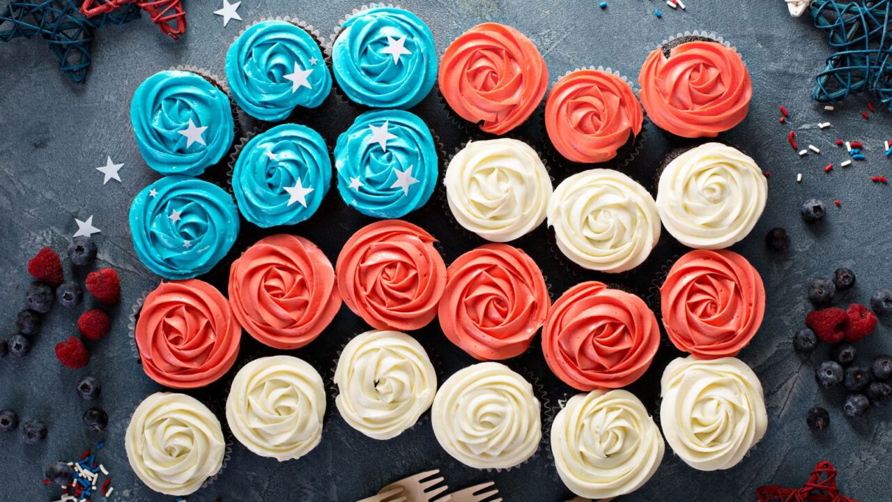 Blue, red, and white cupcakes with star sprinkles with berries and sprinkles scattered on the table.