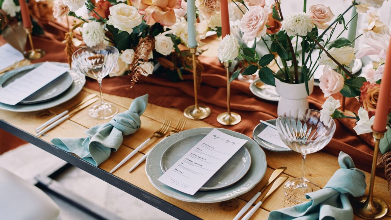 A beautiful table setting with brown table runner, flowers, napkins, candles, and menu cards placed on plates.