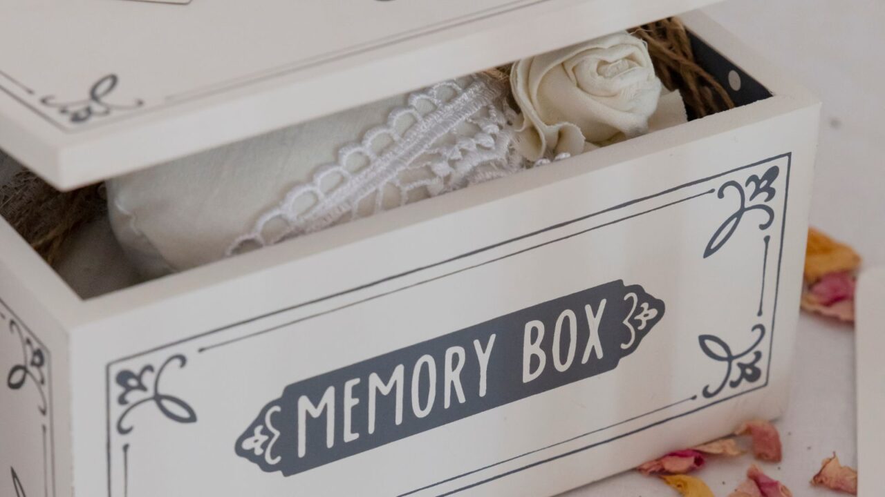 A cute wooden memory box with belongings inside placed on a white surface.