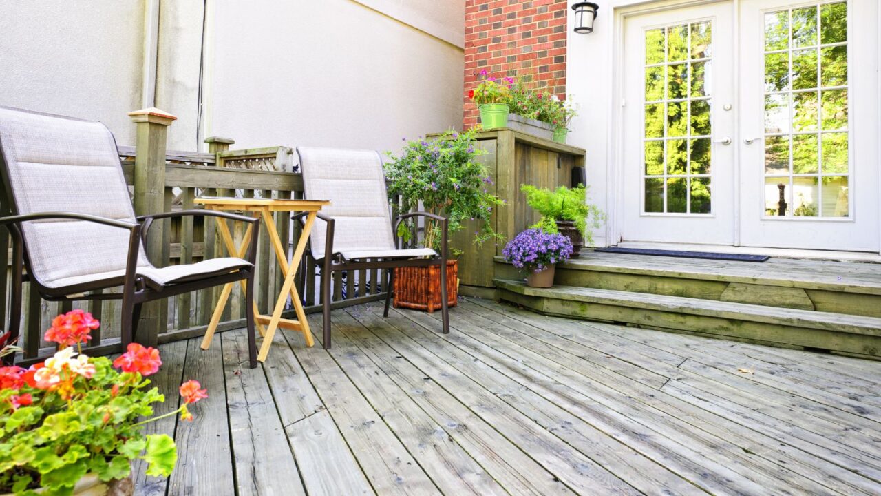 A beautiful patio with a wooden coffee table and metal chairs surrounded by colorful plants.