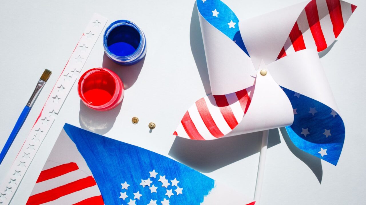A DIY paper pinwheel with paints and brush on a white surface.