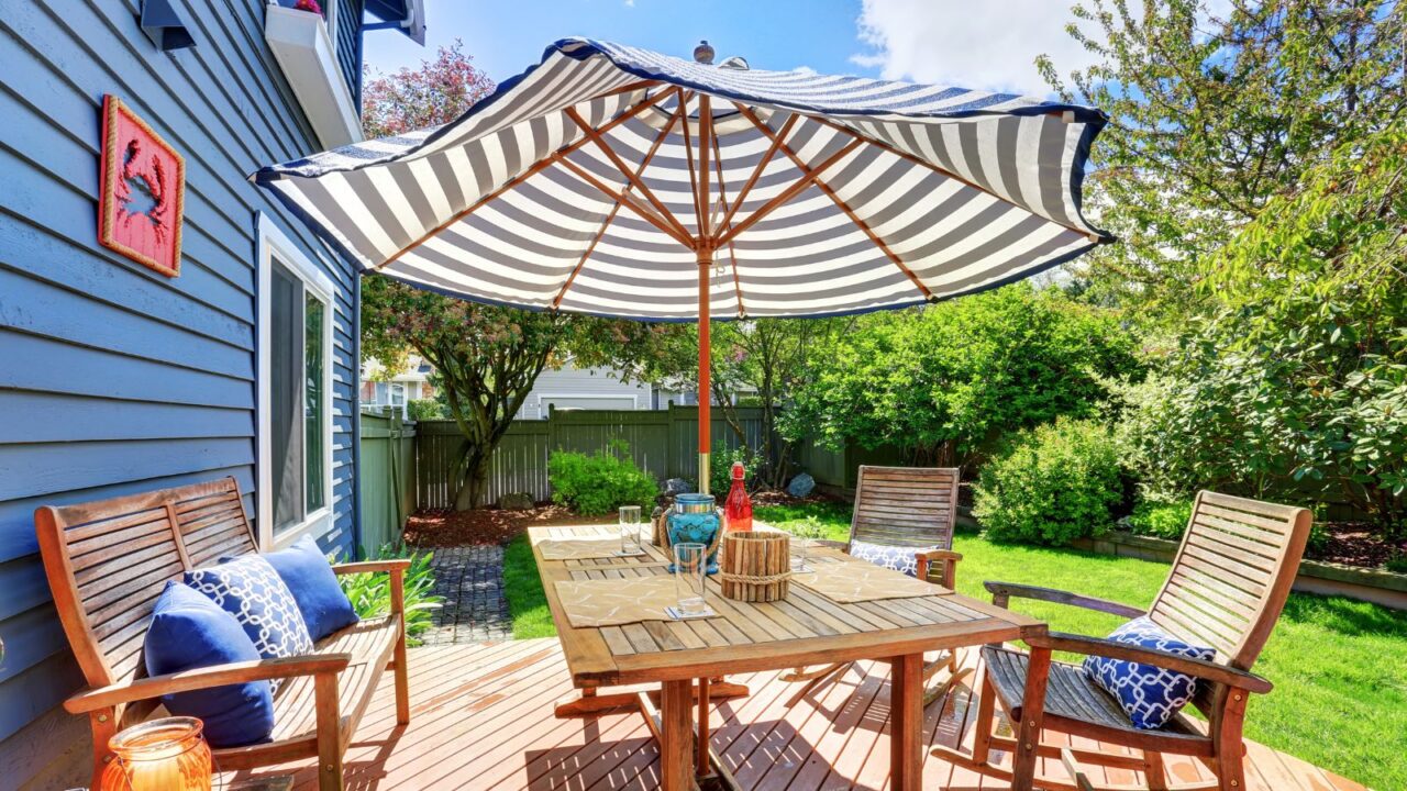 A stylish patio with a wooden table, chairs, throw pillows, and a striped patio umbrella.