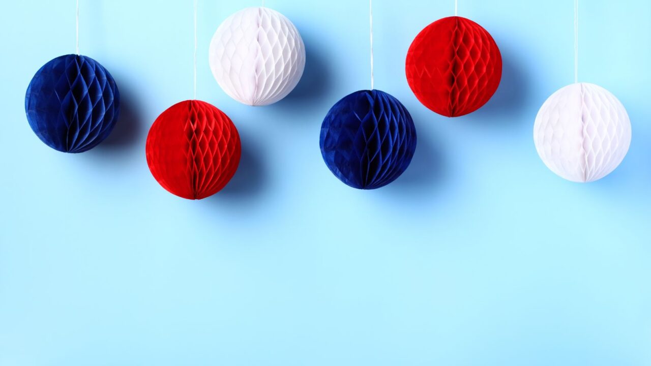 DIY blue, red, and white honeycomb balls hanging with a white thread in front of a blue wall.