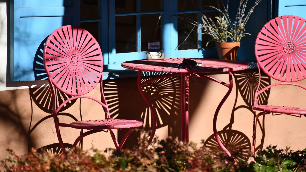 A vintage inspired patio with pink chairs and table in front of a window.