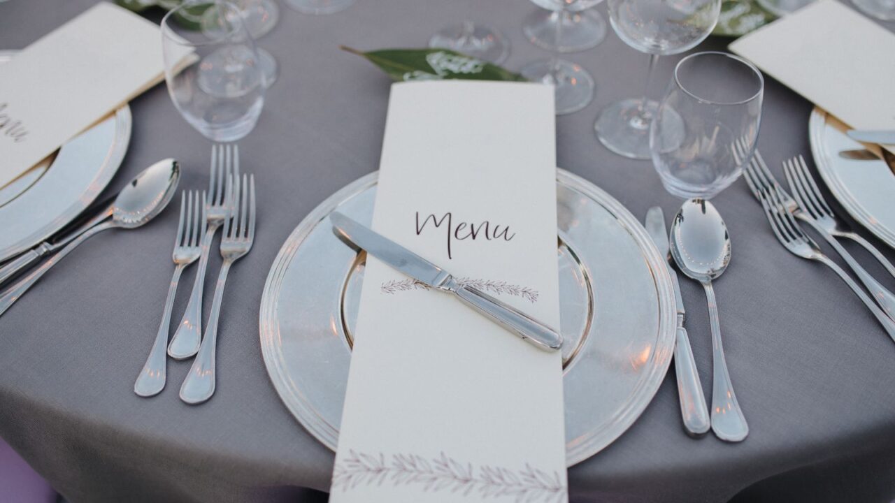 A table with gray tablecloth, stylish dinnerware, and a menu card placed on each plate.