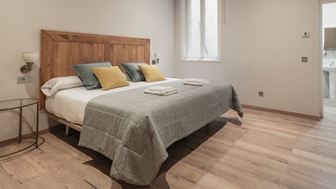A bedroom interior with a bedside table, lamps, and a bed with a diy door headboard on the wooden floor.