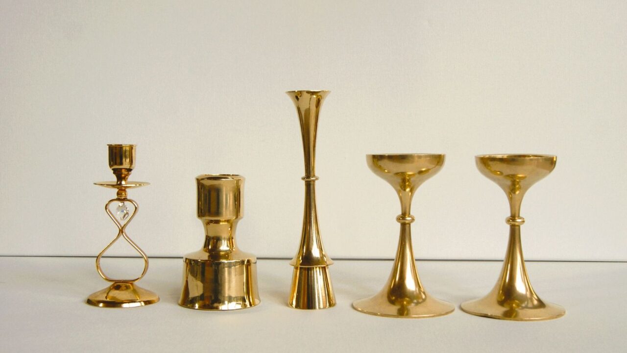 Golden decorative candle holders on a white table in front of a white wall.