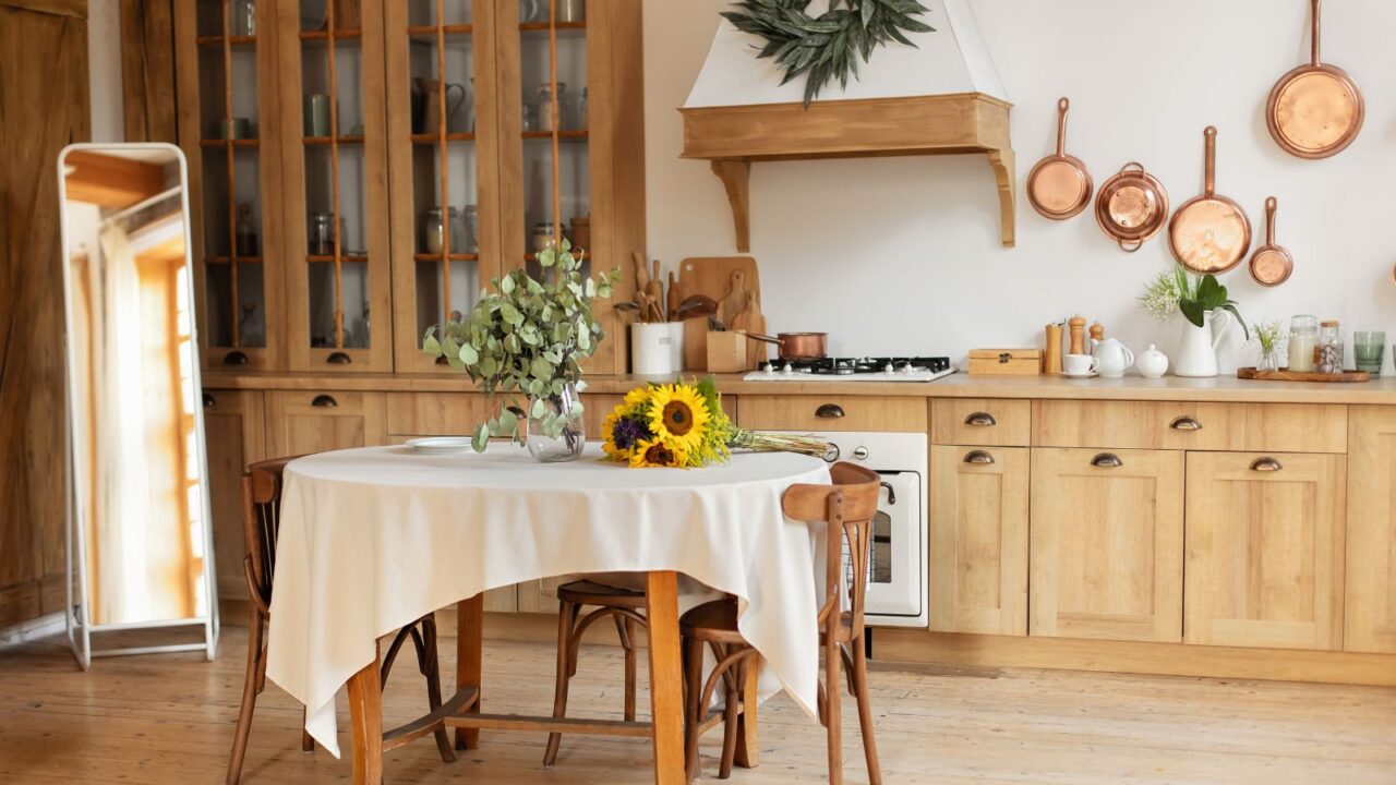 A wooden kitchen interior with a wooden table, chairs, fresh flowers, and a full length mirror.