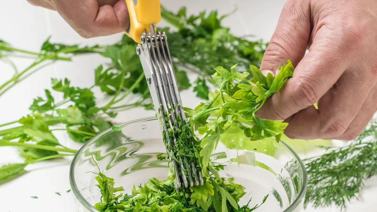 A man cutting herbs using a five-blade herb scissor into a bowl.