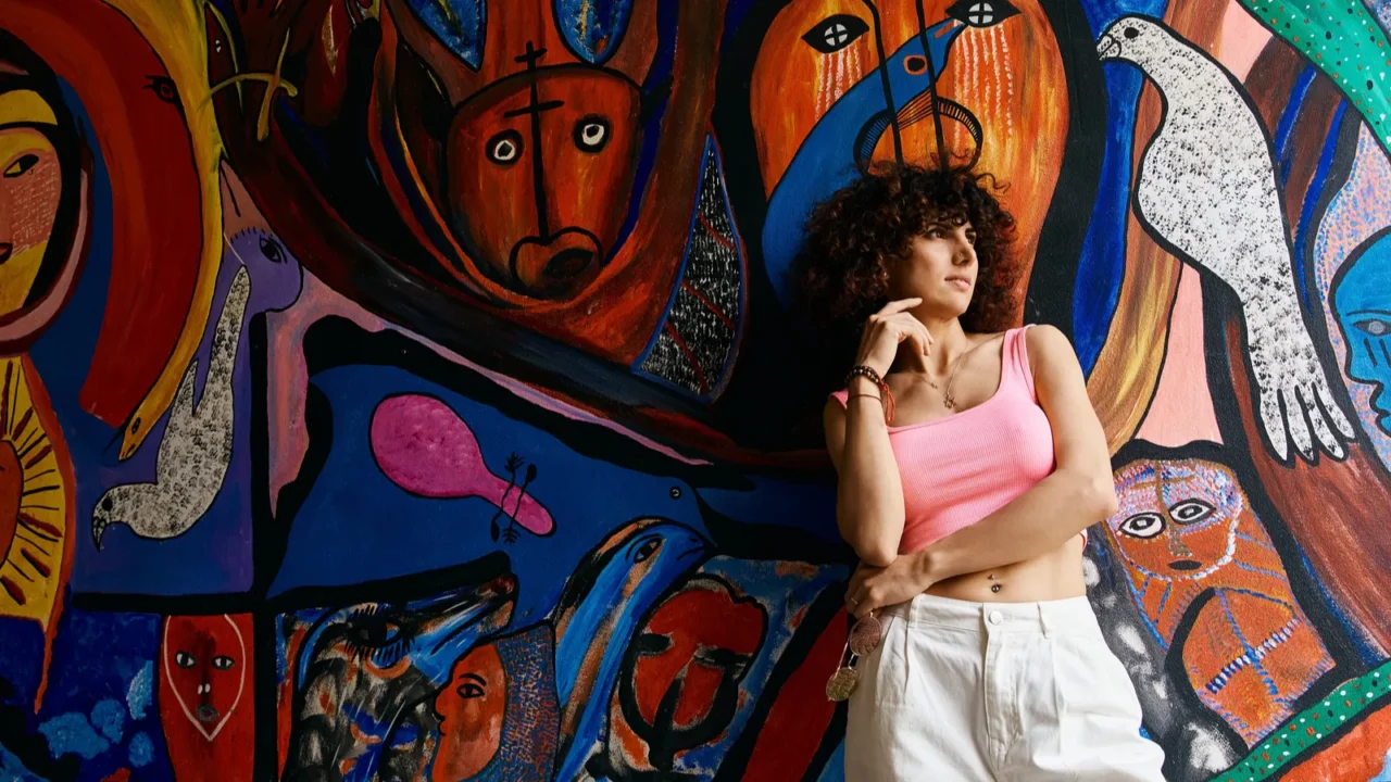 Woman standing infront of a vibrant, abstract art wall background.