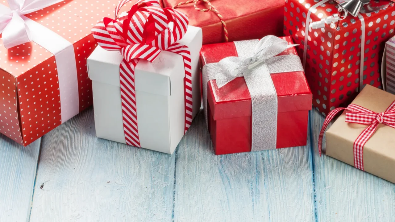Different gifts packed in red and white boxes placed on a wooden table.