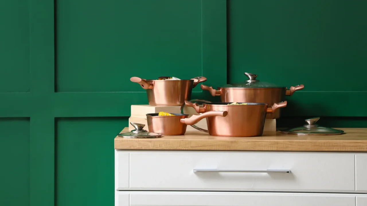 Kitchen with copper pots and pans on a green wall with wooden countertop.