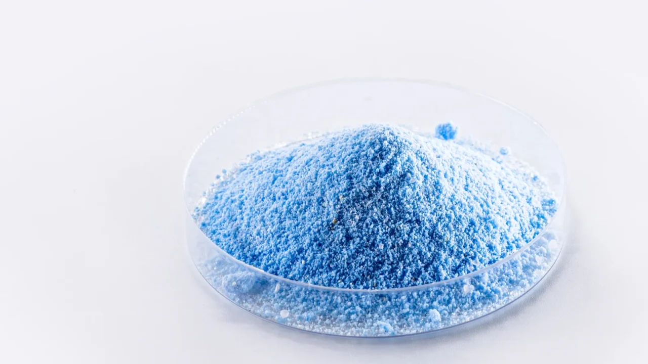 Blue pool chemical powder in a clear plastic dish.