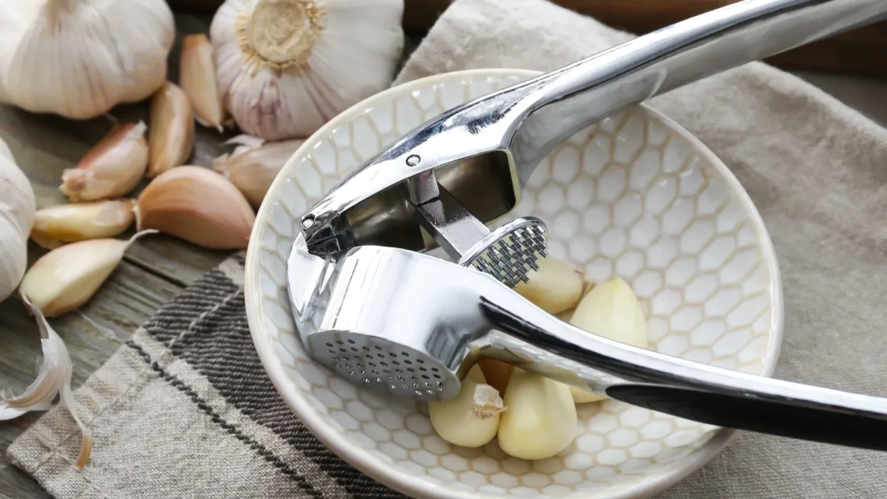 garlic press with bowl and cloves on table