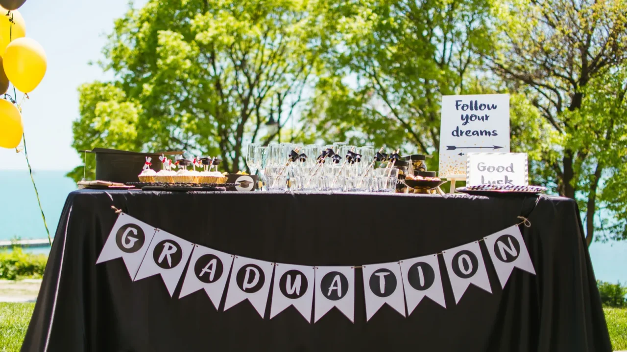 A graduation table setting with glassware, cupcakes with cute toppers, bunting, message board, and balloons.