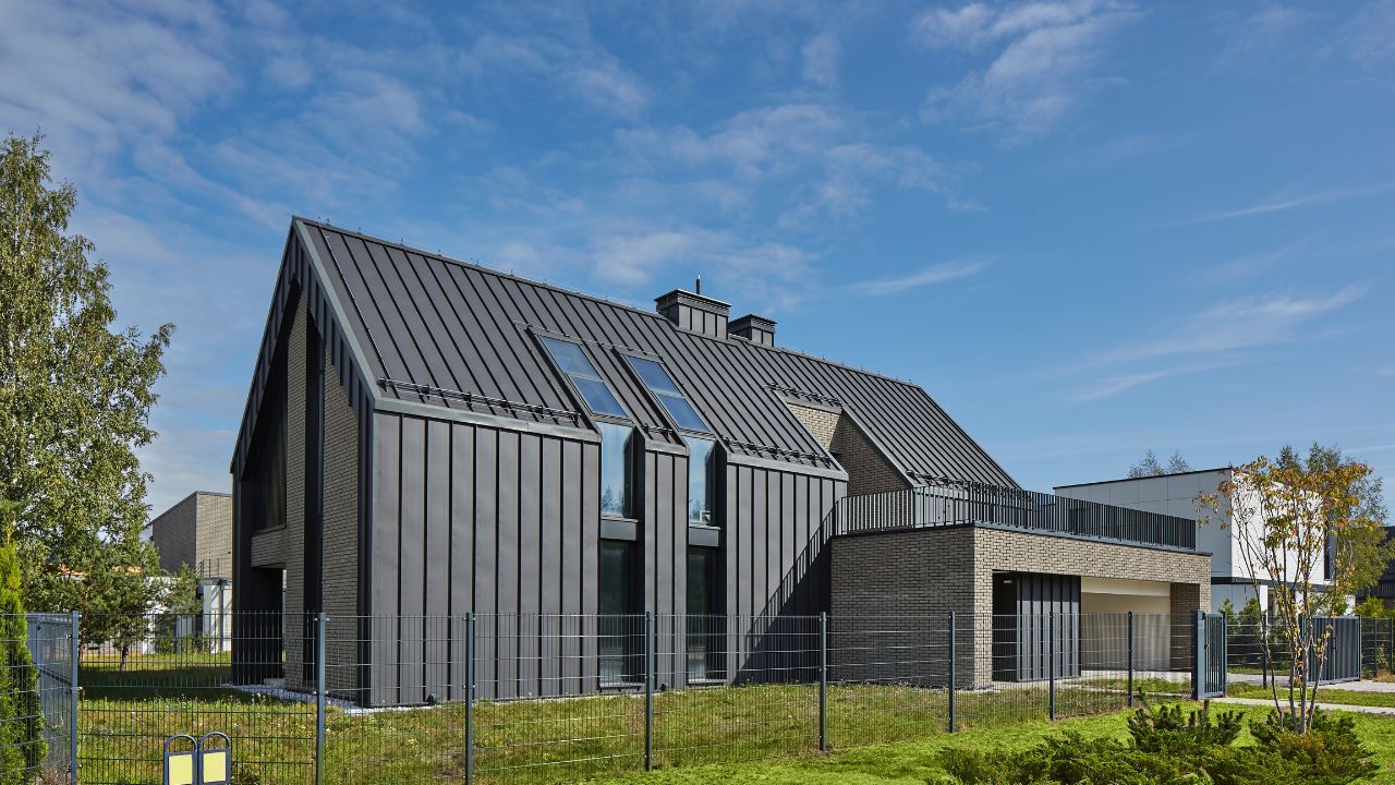 A modern house with a sloped metal roof, large windows, and a sleek black and gray exterior under a clear blue sky.