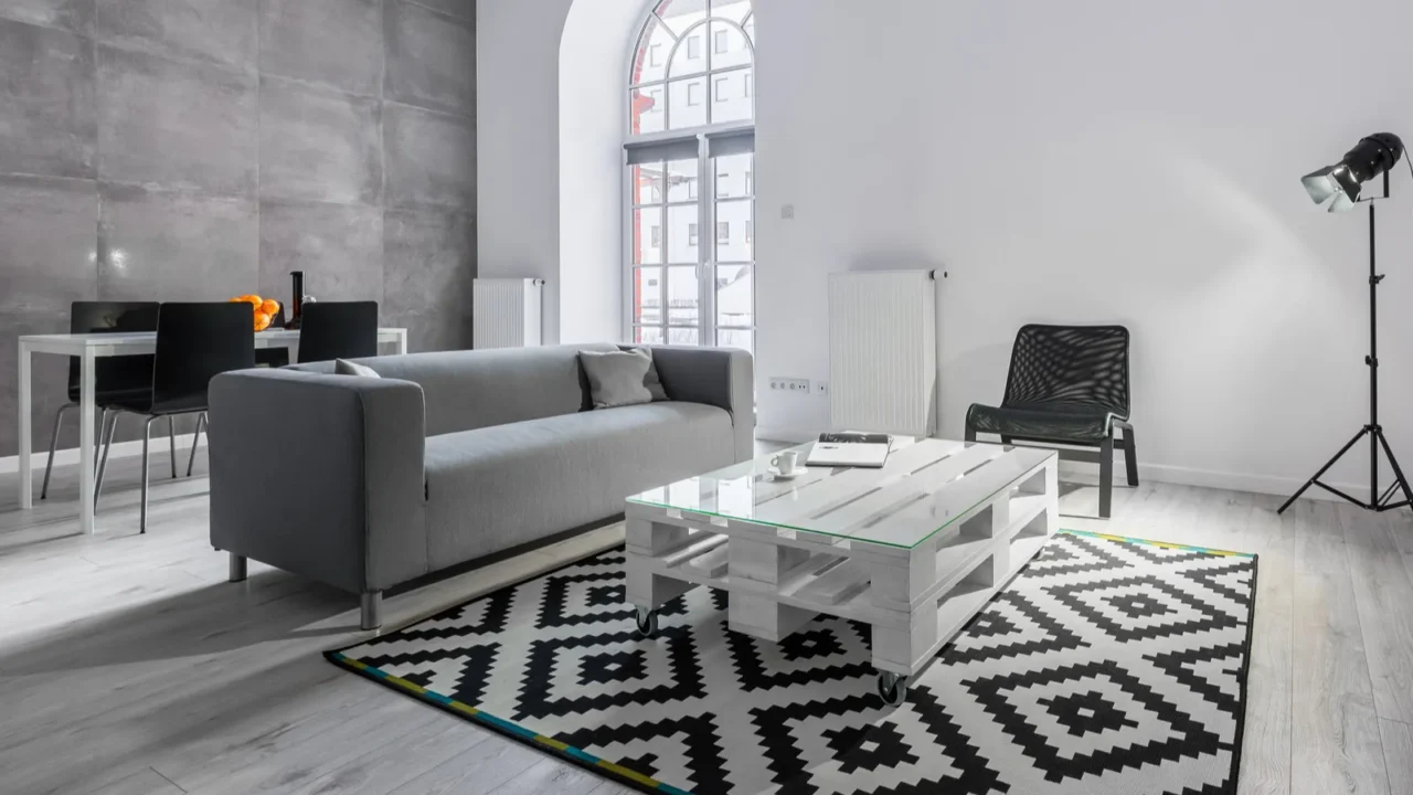 A living room interior with a cozy gray sofa, chair, a wooden pallet coffee table, and a rug.