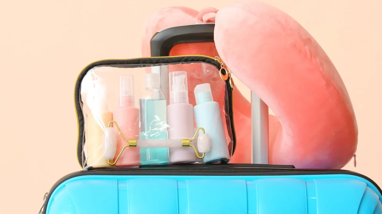 neck pillow travel cosmetics kit and packed suitcase on light