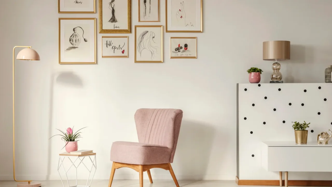 A stylish living room interior with a wooden pink chair, floor lamp, coffee table, gallery wall with golden frames, and gold accents.
