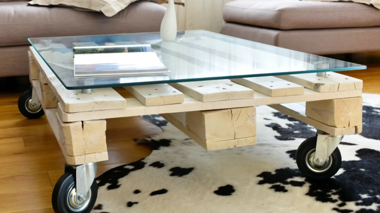 A wooden pallet coffee table with a glass top and wheels on a rug in a living room.