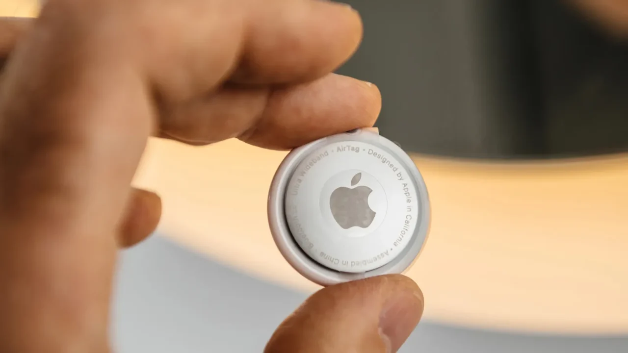 A close-up of a hand holding an Apple AirTag tracking device.