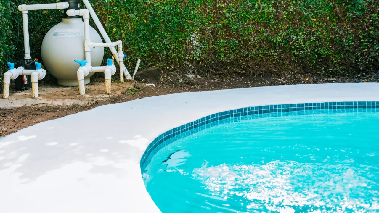 Outdoor pool with a clean, white concrete surround and greenery.