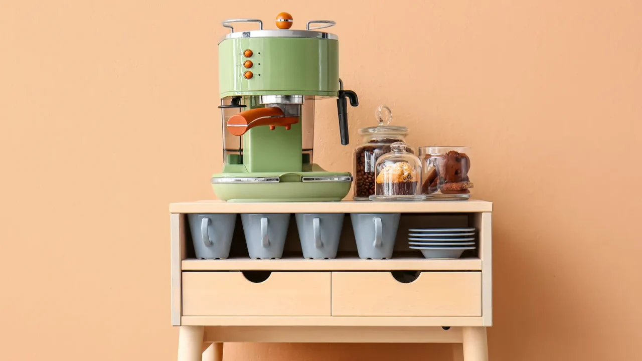 table with coffee machine snacks and cups near beige wall