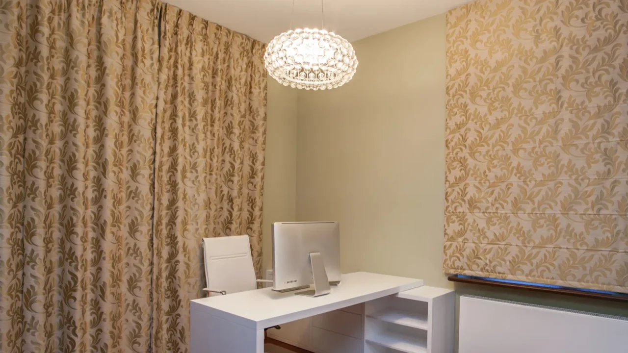 A luxurious home office interior with white desk and chair, printed drapes, and sculptural ceiling light.
