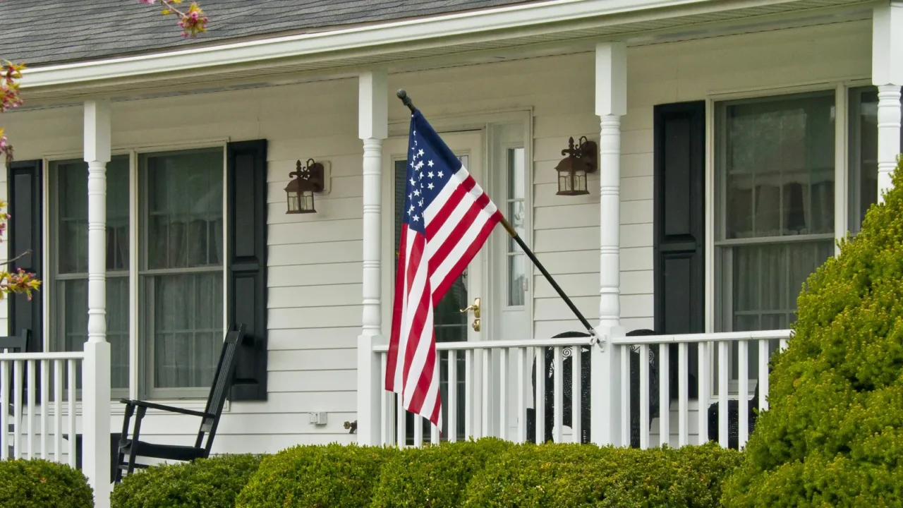 A white porch with chair, wall sconces, and an American flag.