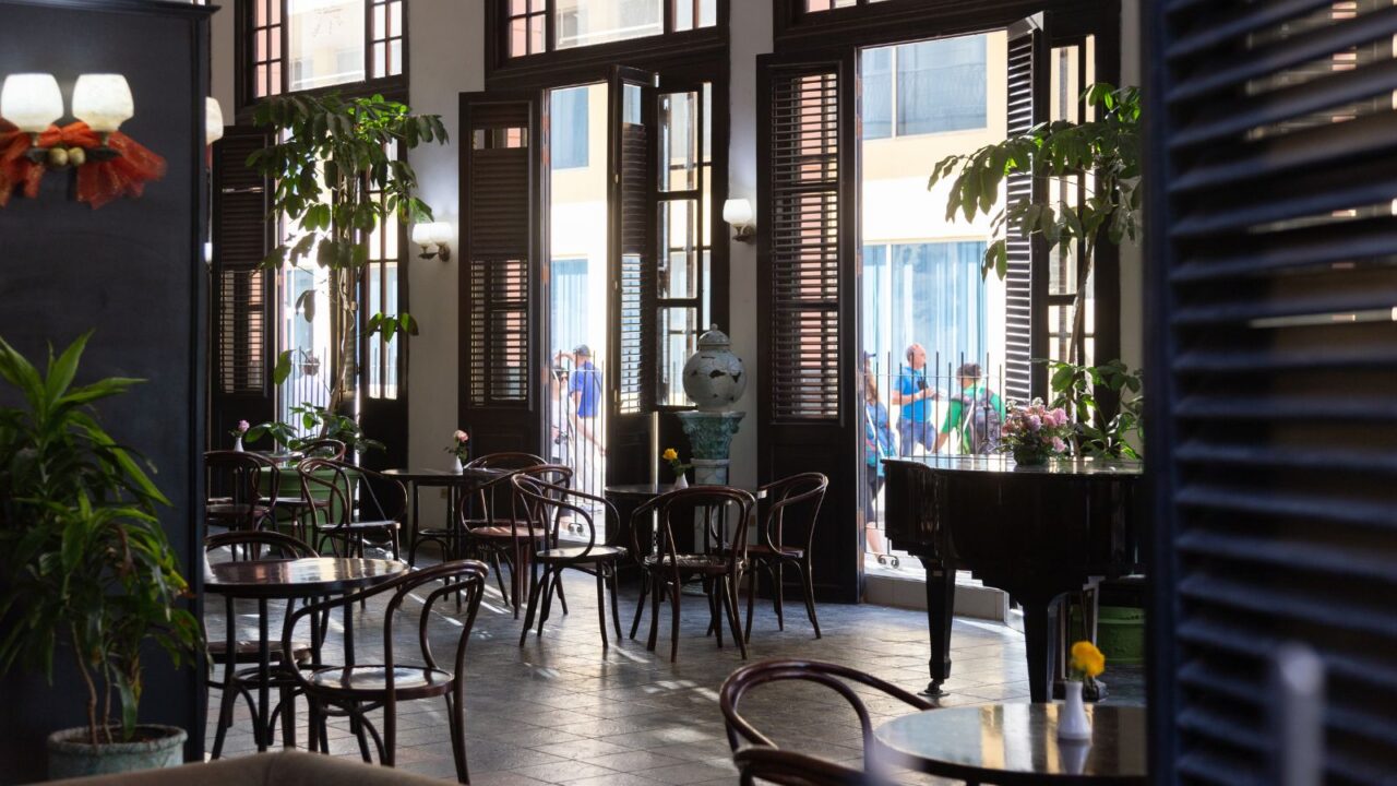 A cozy interior with dark wooden furniture and large windows, showing people outside.