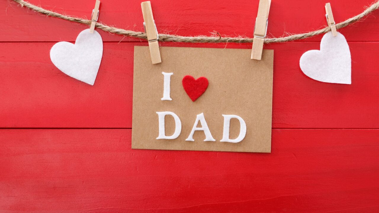 Fathers day message with felt hearts hanging with clothespins over red wooden board.