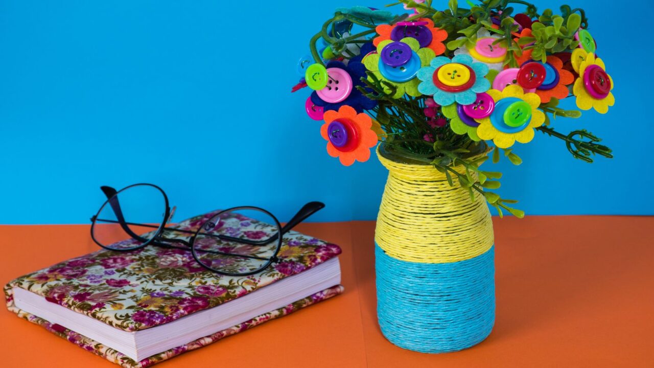 A bright bouquet of button and felt flowers in a striped yellow and blue vase.