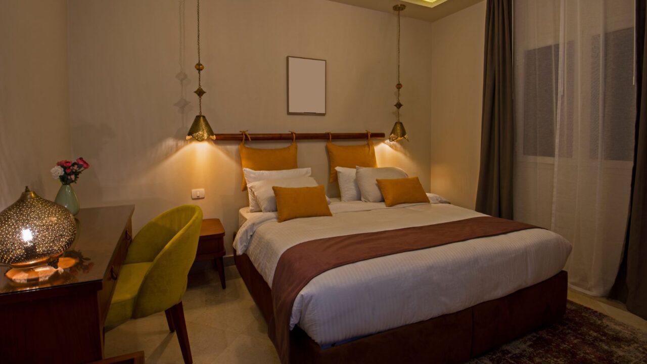 A cozy bedroom with warm lighting, decorated with pillows and a bedside table.