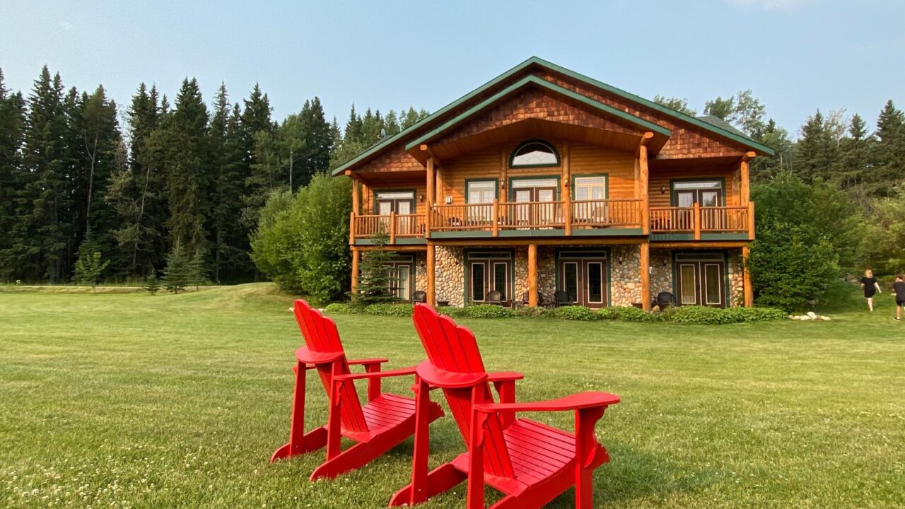 Red Adirondack chairs on the grass in front of a rural chalet.