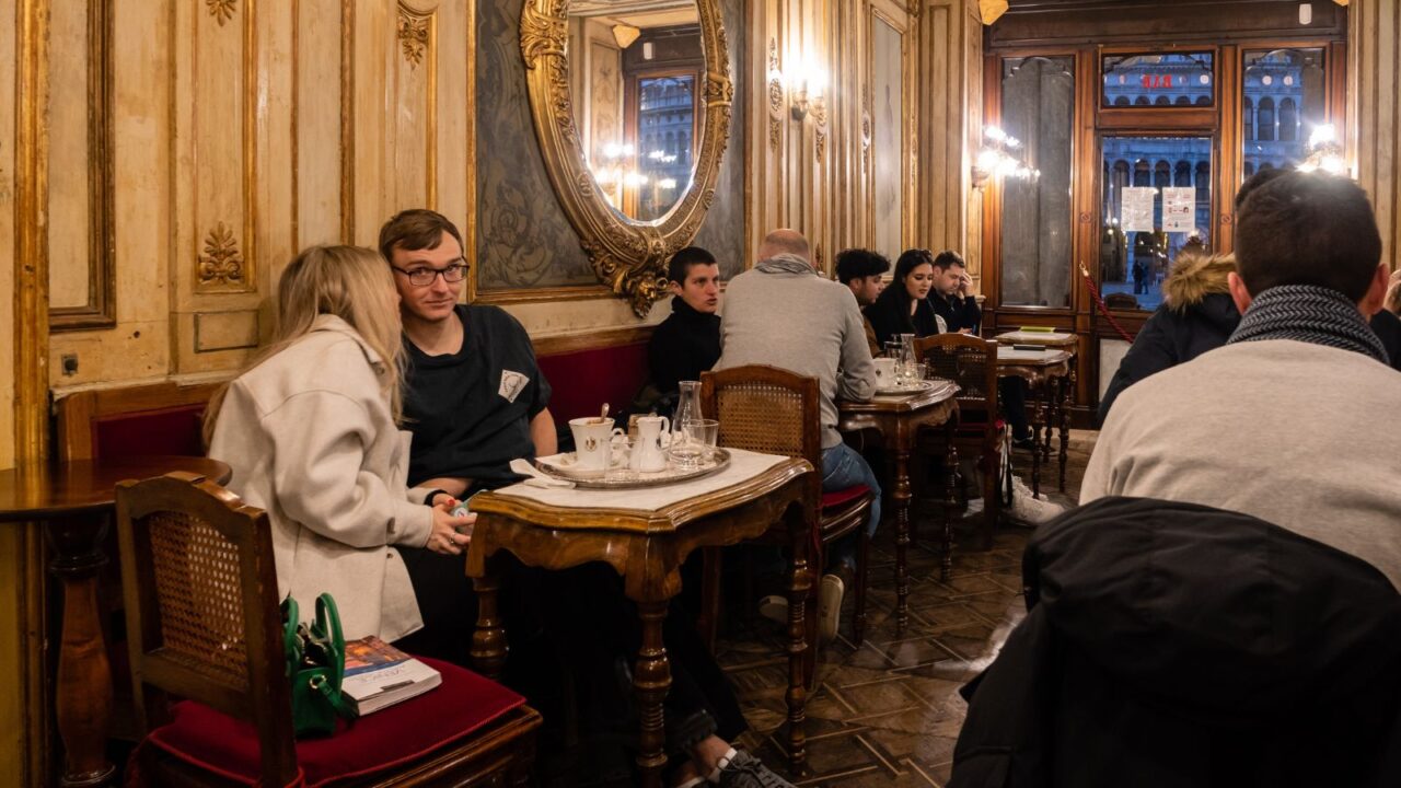 A warm, vintage-style café with wooden walls and red cushioned seats, filled with patrons.