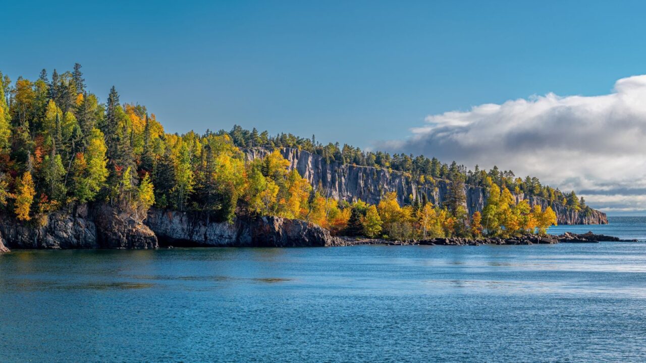 As clouds build over Lake Superior, the fall colors of the Minnesota northwoods shine bright against the rugged coast.