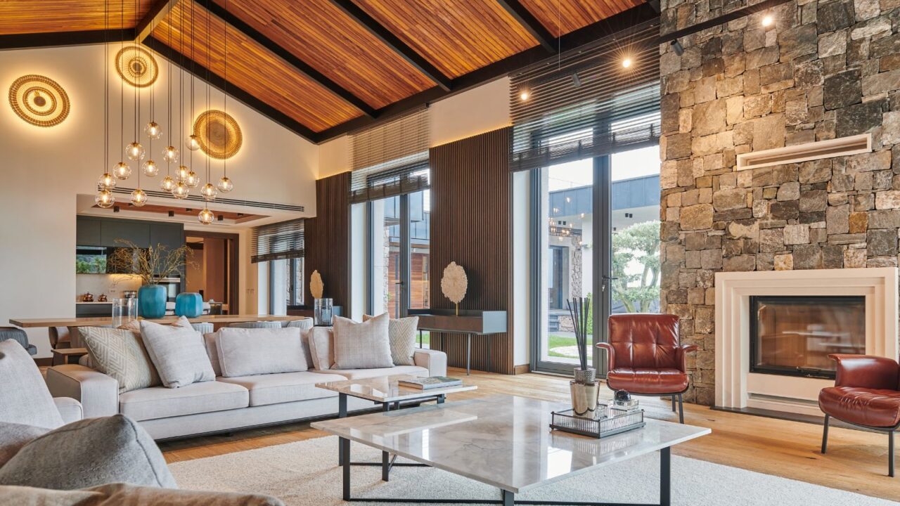 An open-concept living room with a vaulted wooden ceiling, large windows, and contemporary furniture.