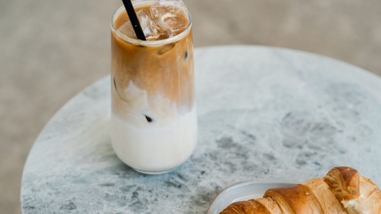 An iced coffee with milk and a croissant on a marble table.