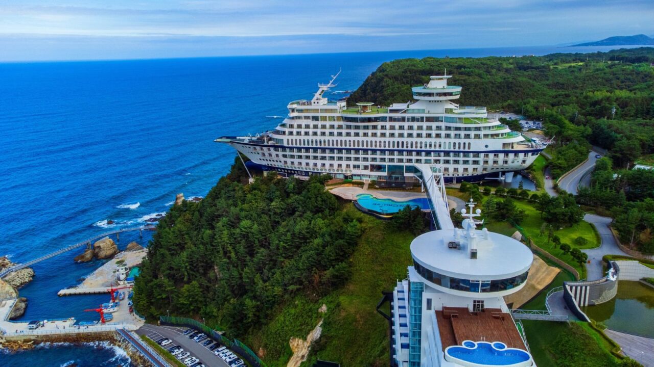 The Sun Cruise Resort in Jeongdongjin, South Korea, with its ship-like structure anchored on a scenic coastline surrounded by greenery.