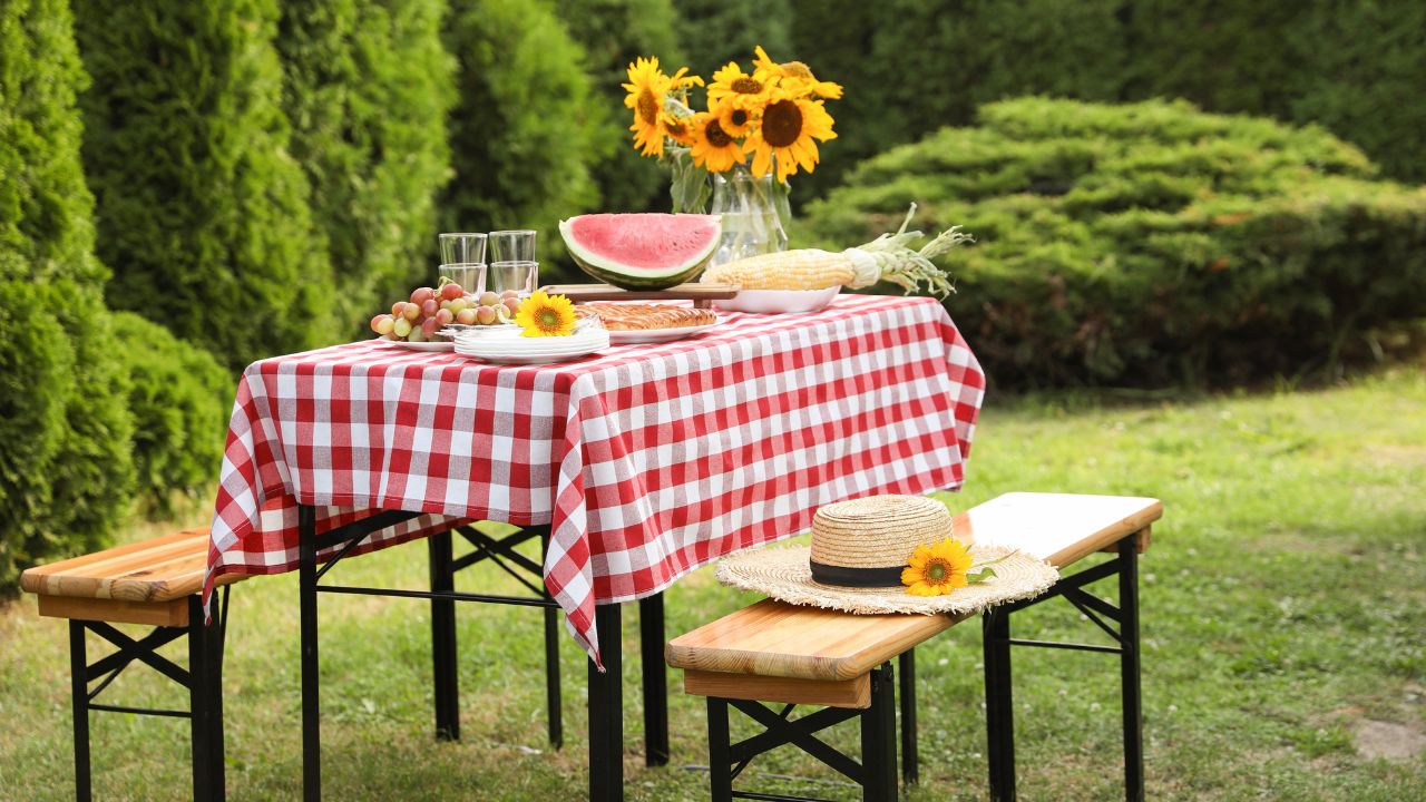 An outdoor picnic table with watermelon, sunflowers, and other foods, set on a grassy lawn.