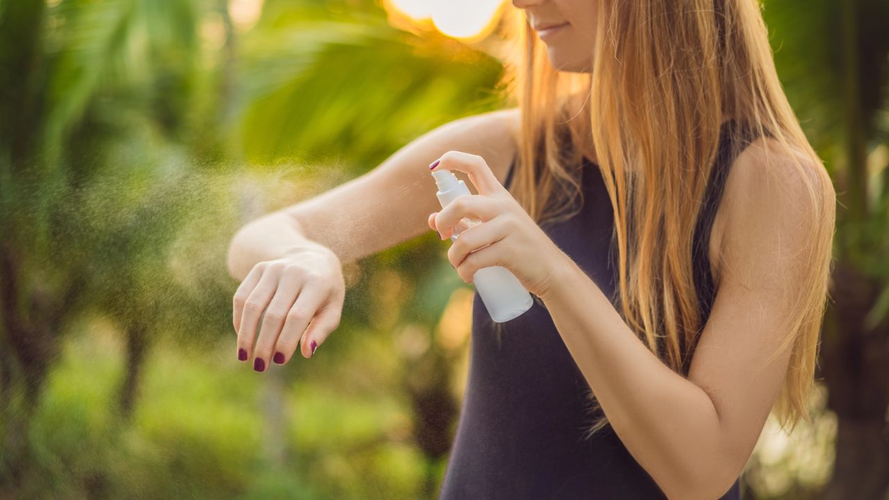Woman spraying lotion or sanitizer on her arm outdoors.