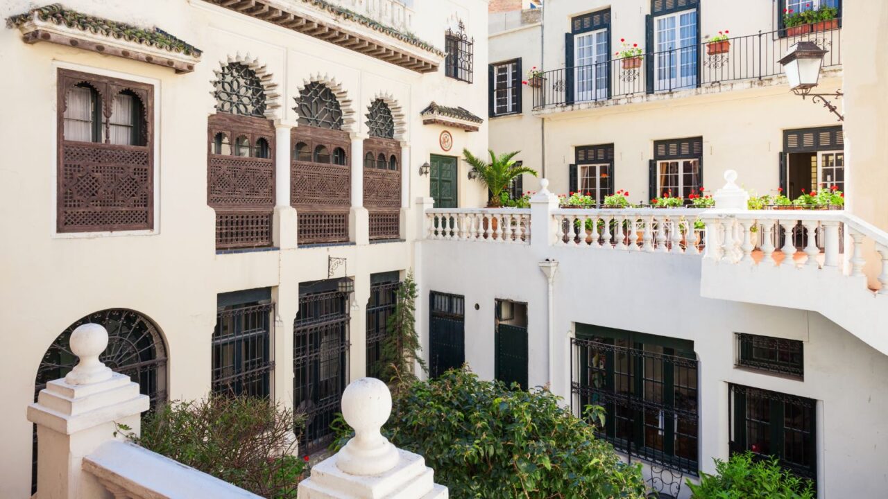 A charming white colonial-style building with balconies, potted plants, and decorative windows and railings.