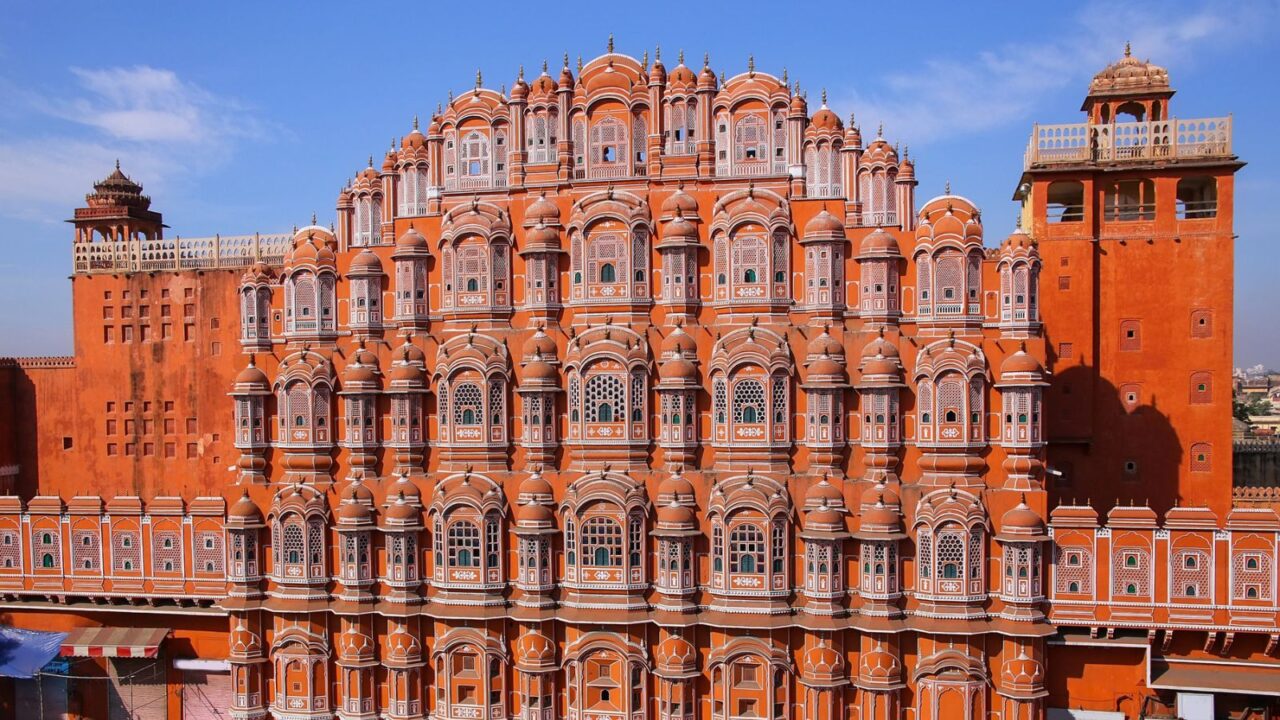 A stunning view of the Hawa Mahal in Jaipur, India, with intricate pink sandstone lattice work and multiple windows under a clear blue sky.