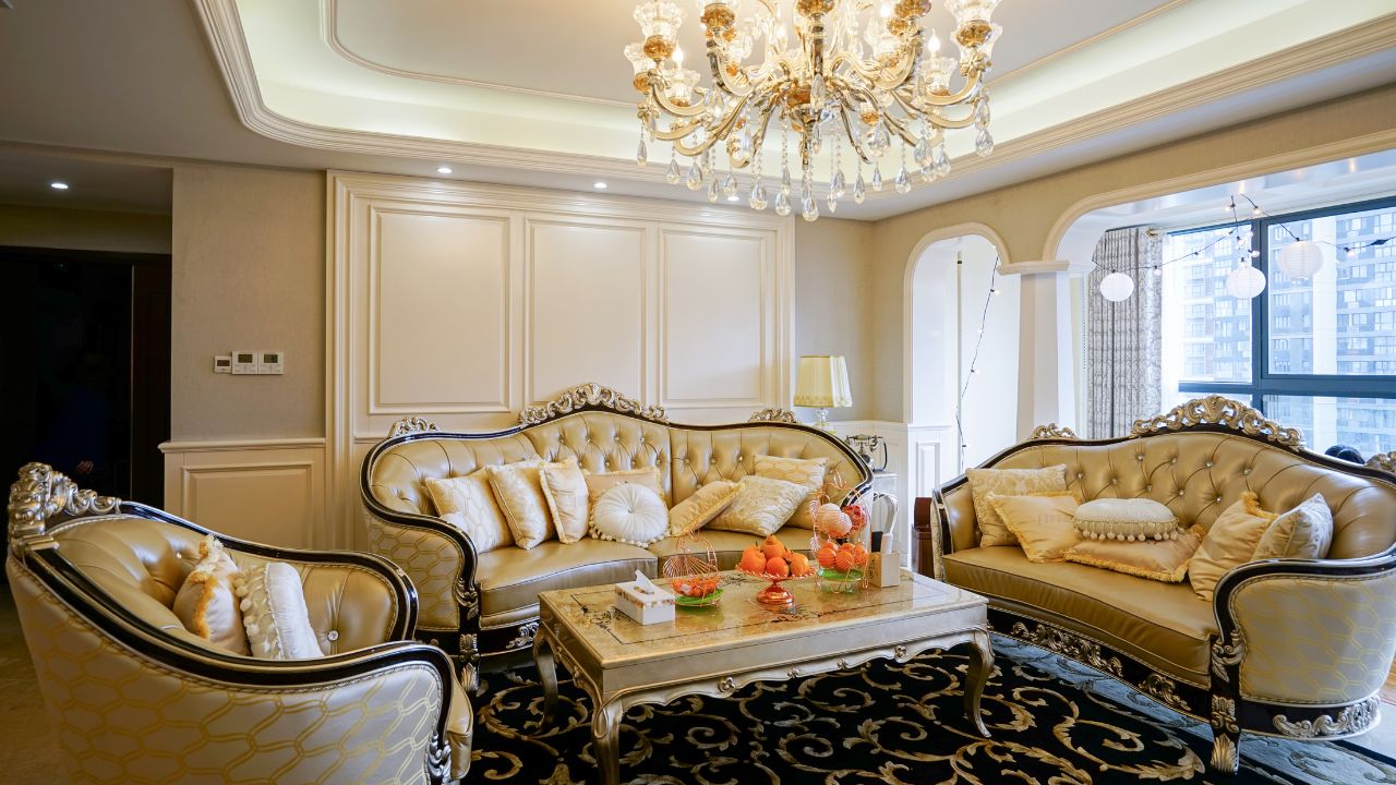 An elegant living room with matching sofas, a marble coffee table, chandelier, and city view through large windows.