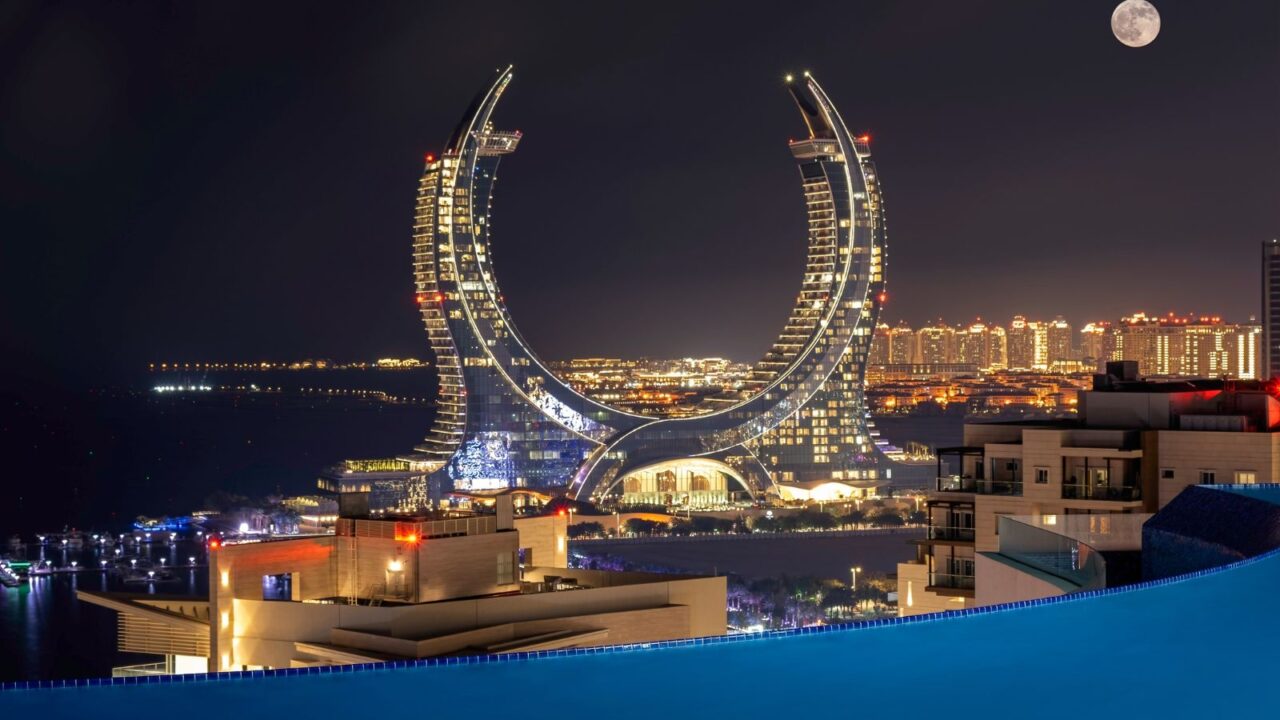 The futuristic Katara Towers in Lusail, Qatar, illuminated against the night sky with the moon visible above.