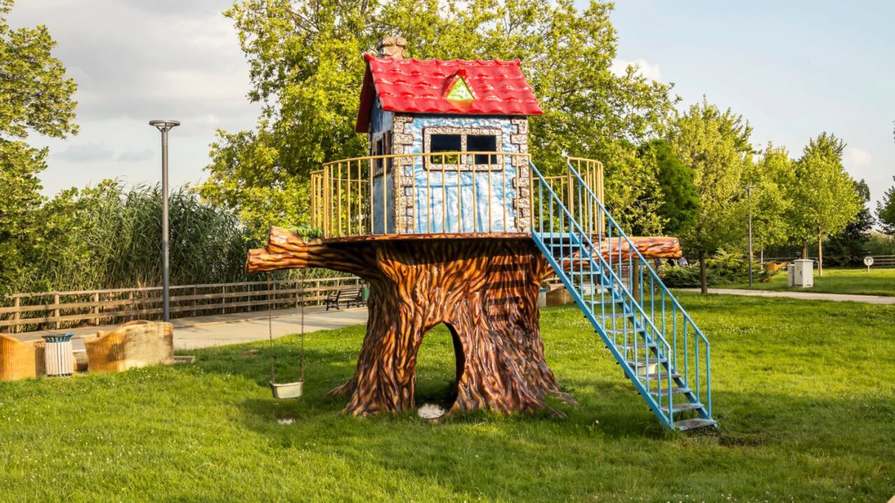 A colorful outdoor playset featuring a slide, climbing wall, and treehouse in a well-maintained backyard.