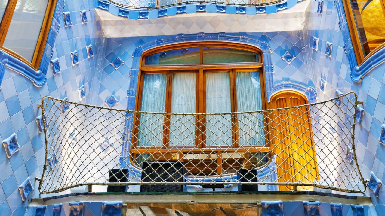 Casa Batlló’s inner courtyard showcases glossy blue tiles, curved wooden windows, and a netted balcony that blends function with Gaudí’s whimsical design.
