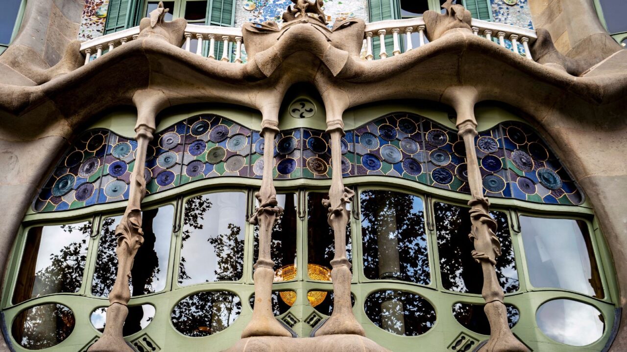 Architectural detail of Casa Batlló in Barcelona, showcasing unique organic shapes, colorful stained glass windows, and intricate stonework.