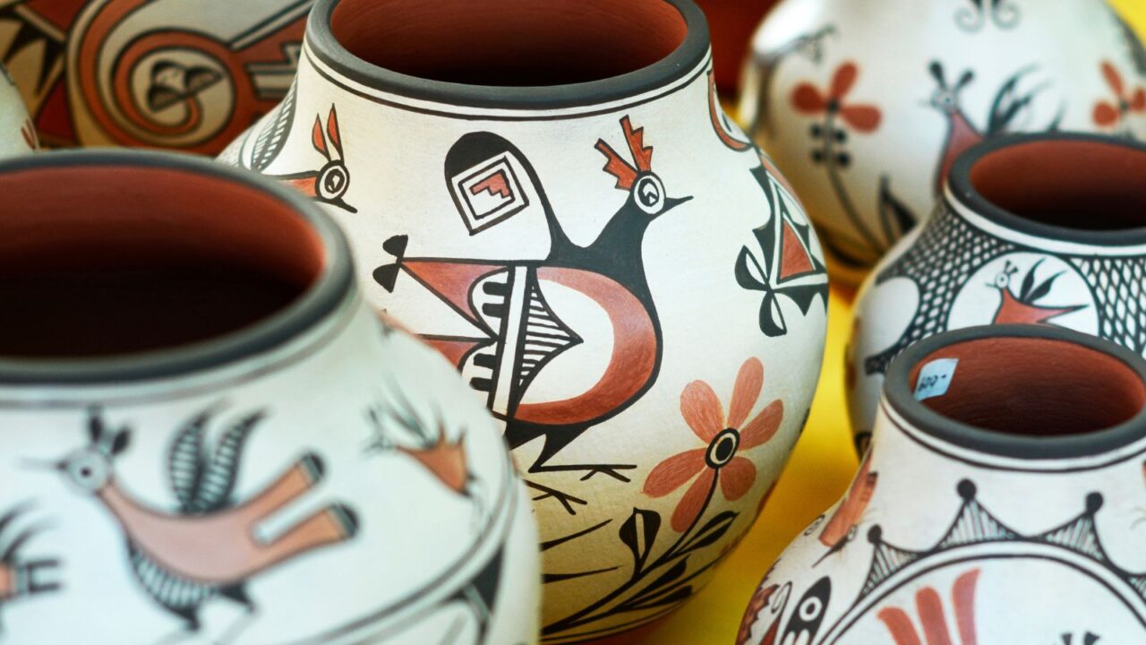 A collection of traditional Native American handmade pottery, likely Zia Pueblo, featuring intricate hand-painted designs including birds and geometric patterns, arranged closely together on a yellow surface.