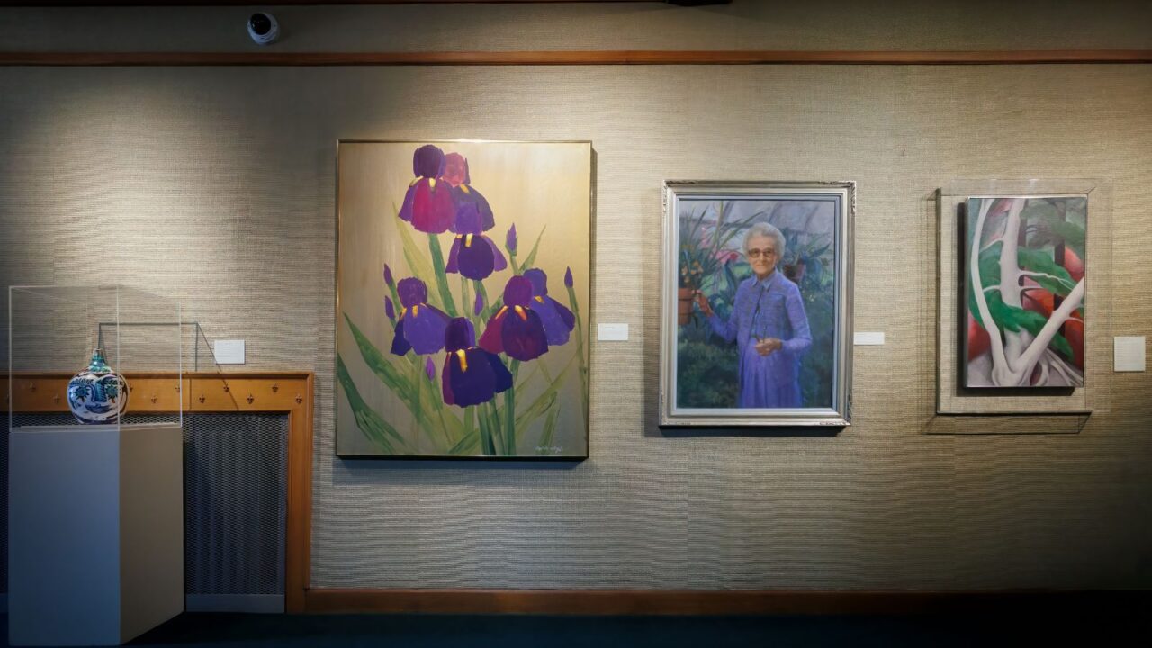 A gallery wall features a ceramic vase, a painting of purple irises, a portrait of an elderly woman in blue, and an abstract artwork with bold organic shapes.